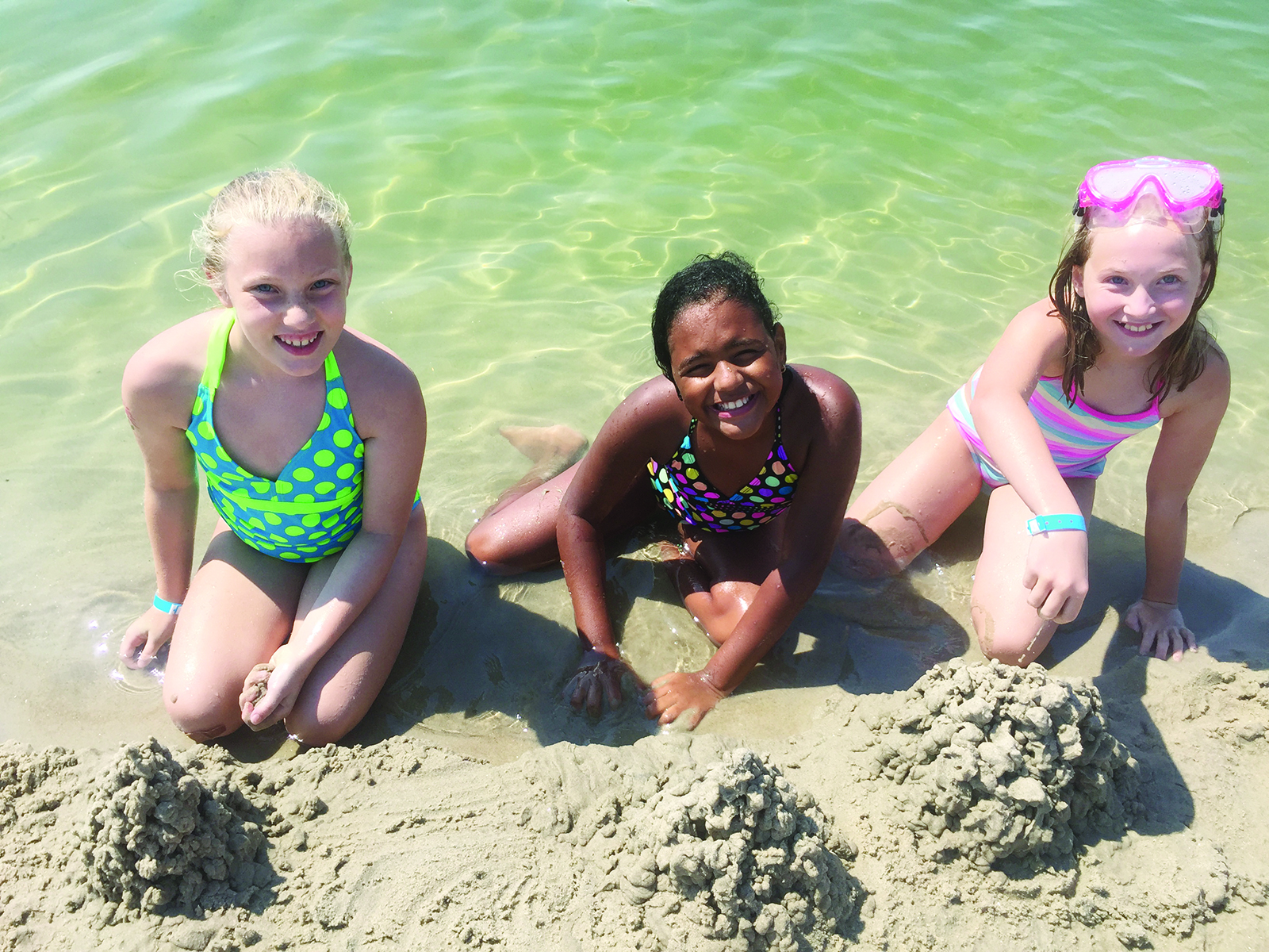Three smiling children with sandcastles on the beach at Crane Beach