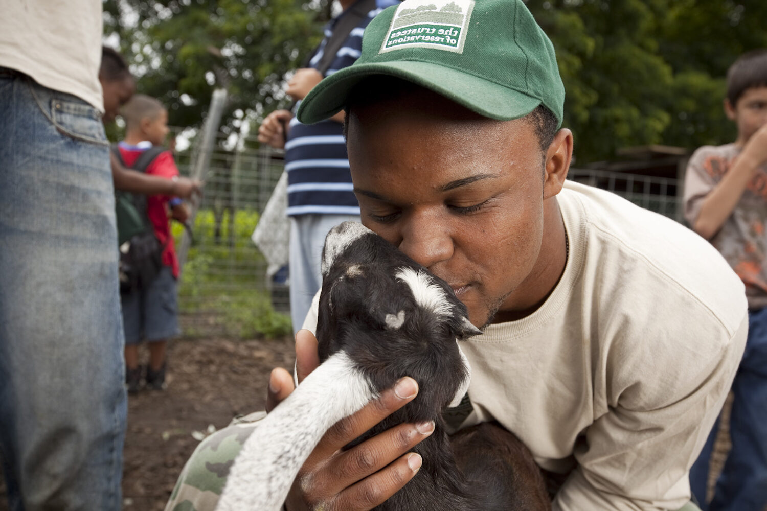 A man holding a baby goat close to his face at a Trustees property