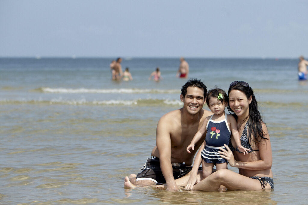 Two smiling adults sitting on Crane Beach with a child during the day