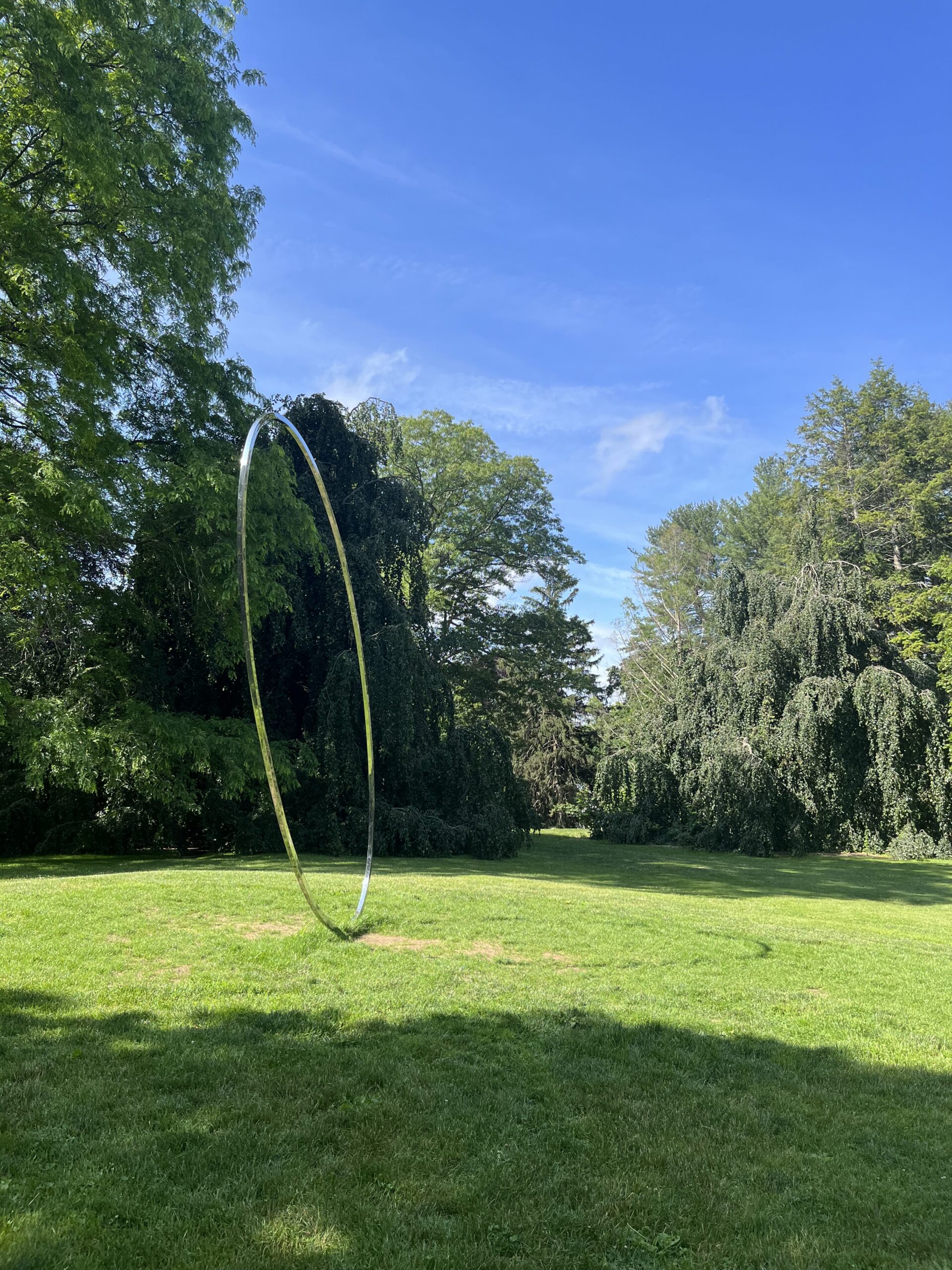 a large elliptical sculpture on a green lawn with blue sky and trees in the background