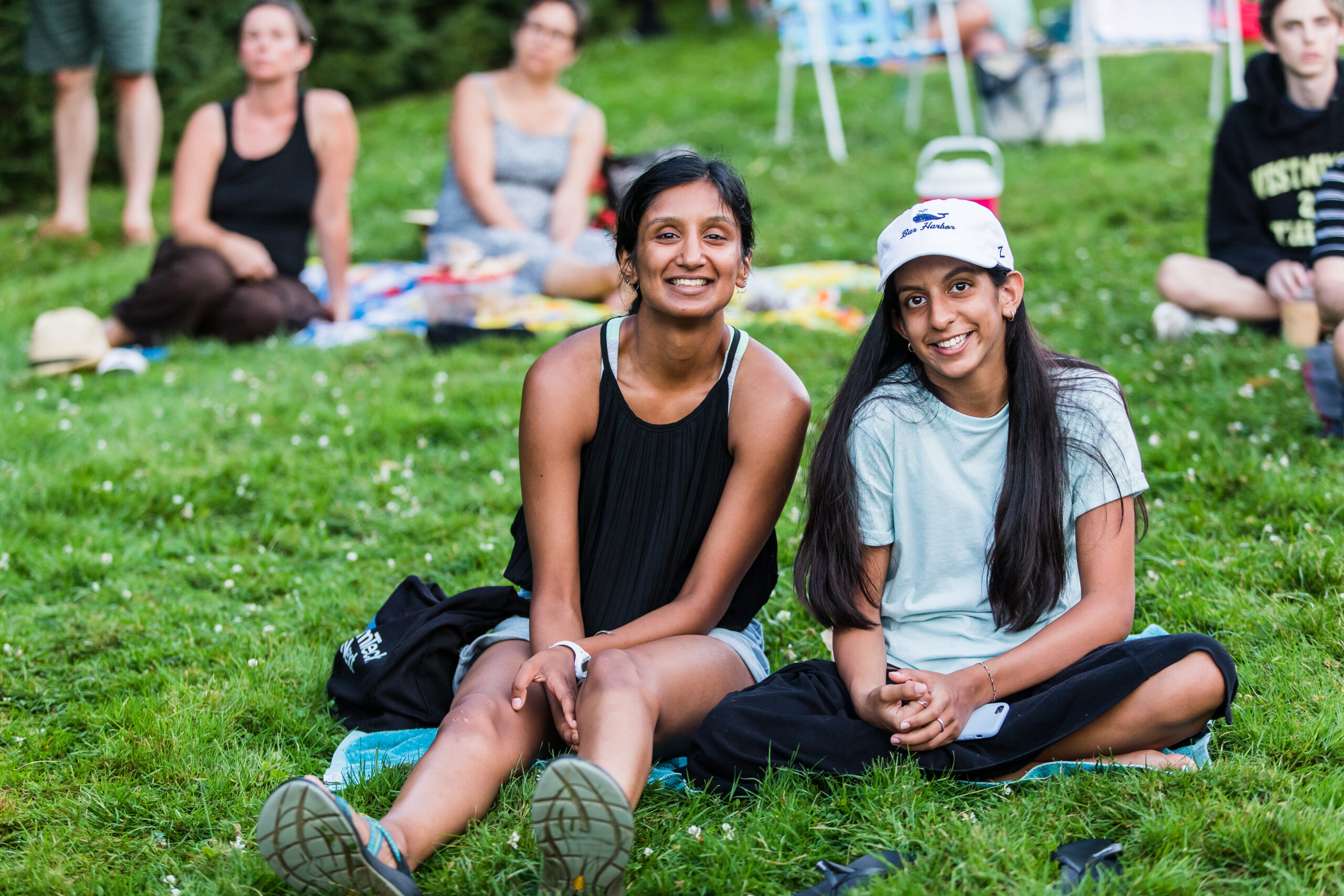 Two smiling people sitting on a blanket on a green lawn at a Trustees outdoor concert