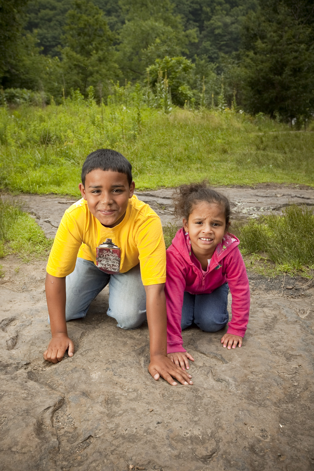 Two smiling children crouched on the ground at Dinosaur Footprints