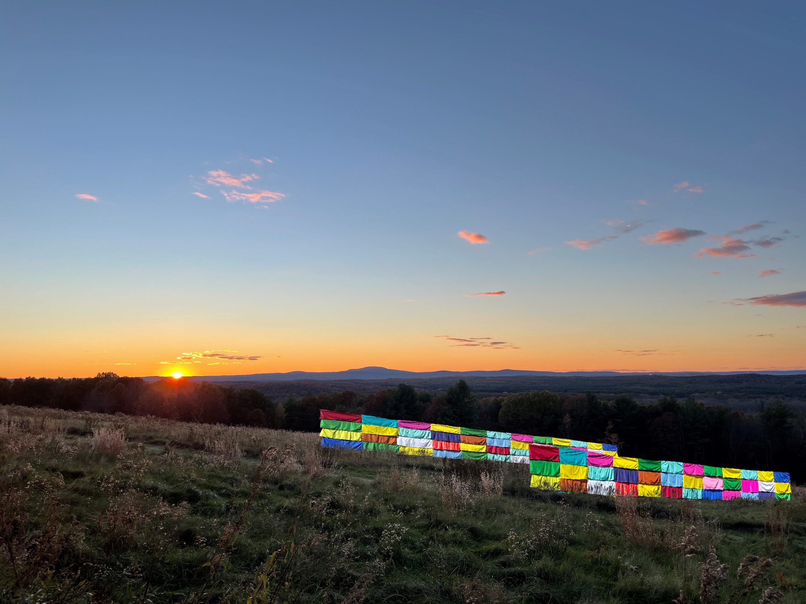 colorful fabric is displayed against a hillside sunset at Fruitlands Museum