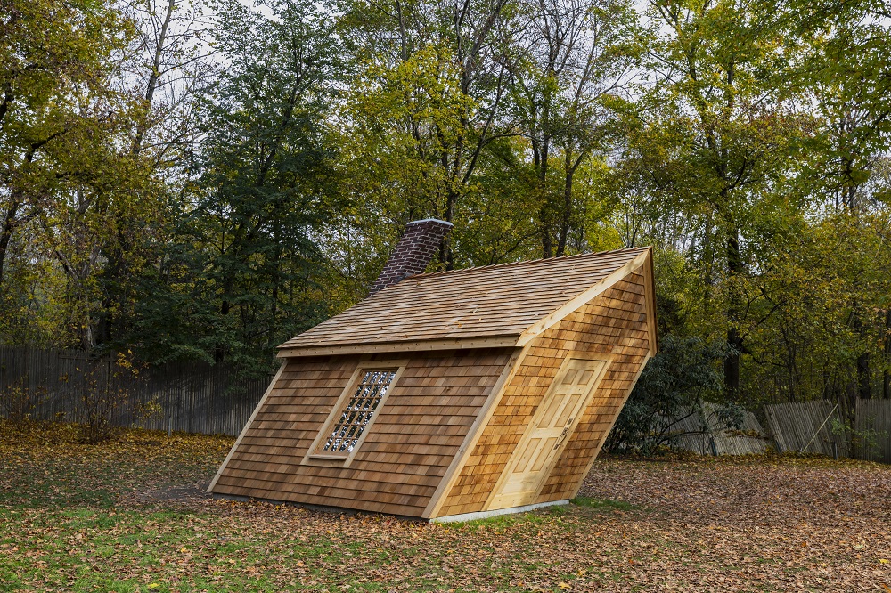 A slanted cabin with shingles and a brick chimney in the style of Thoreau's cabin at Walden