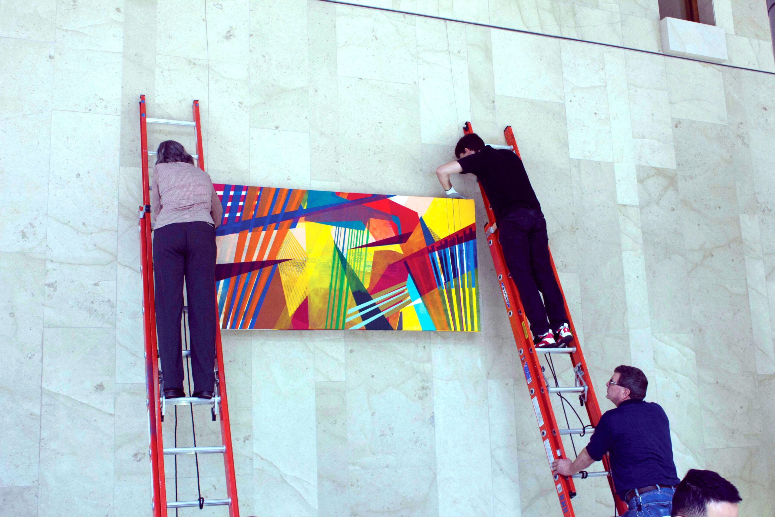 Three people hanging a colorful painting on a wall as part of deCordova's Corporate Art Loan Program