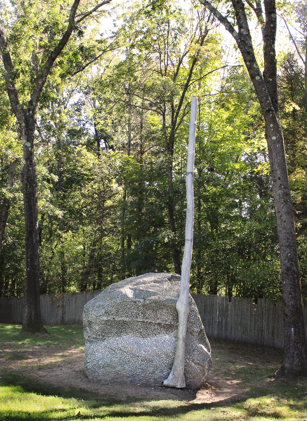 a sculpture of a rock and tree against live trees and green grass
