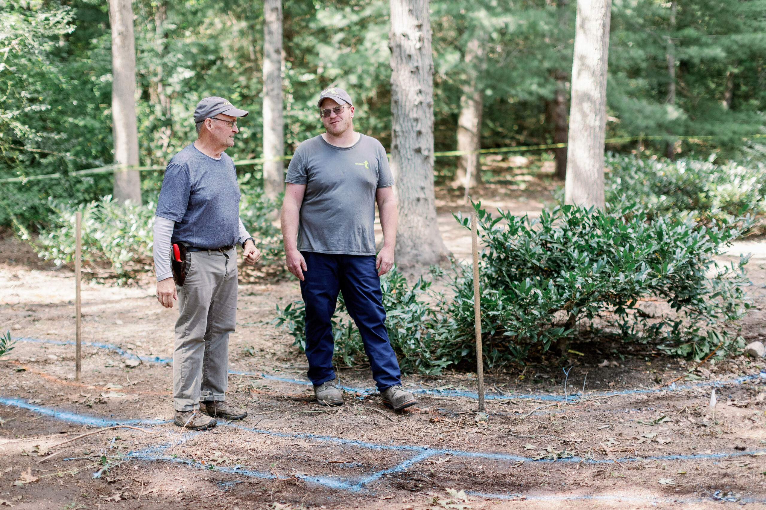 Two men stand talking in a forest area