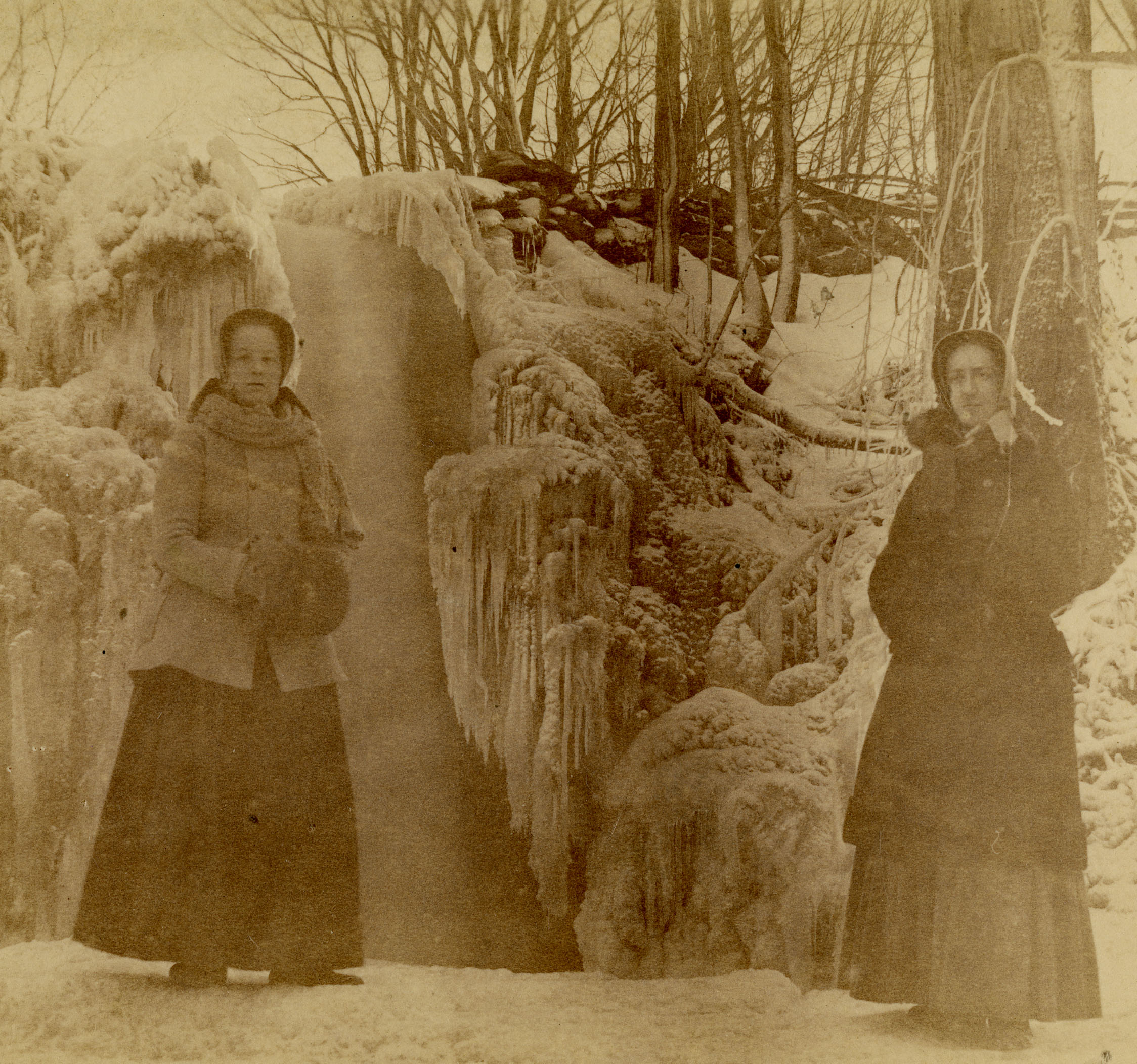 A sepia photo of two Shaker women standing in front of a frozen waterfall