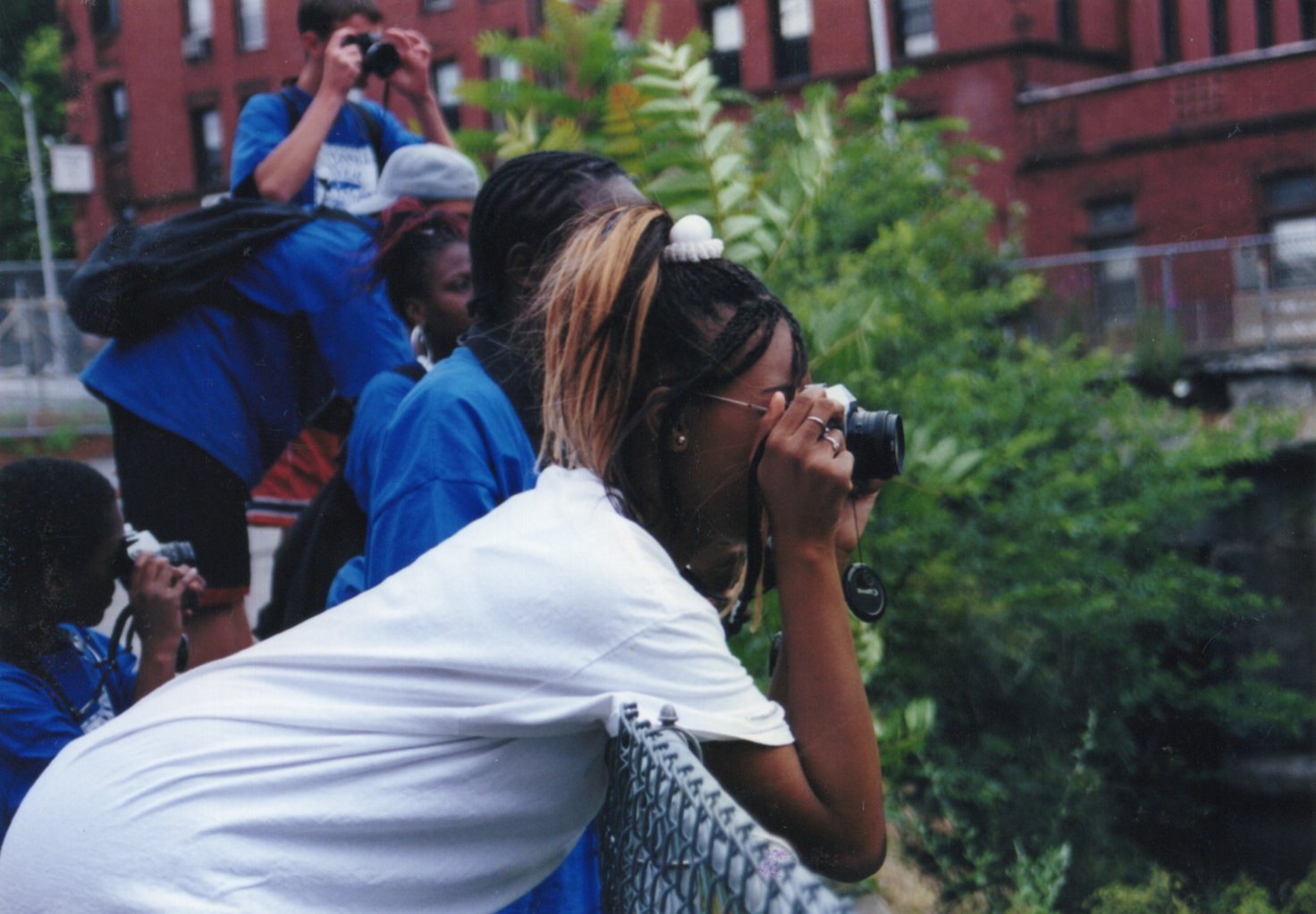 a young black women in a grey shirt leans over a railing to take a photo