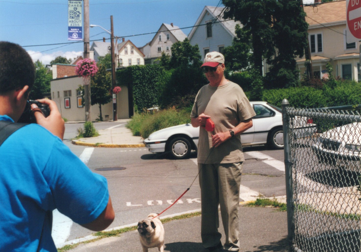 a youth in a blue shirt takes a photo of an older man and his dog