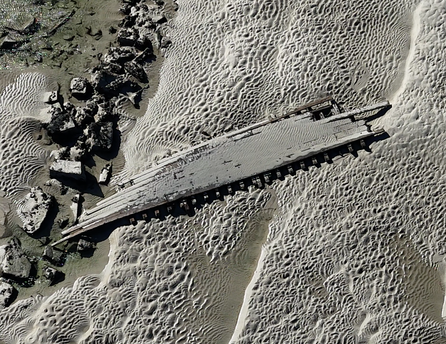 An aerial view of a shipwreck that rests on a sandy beach.