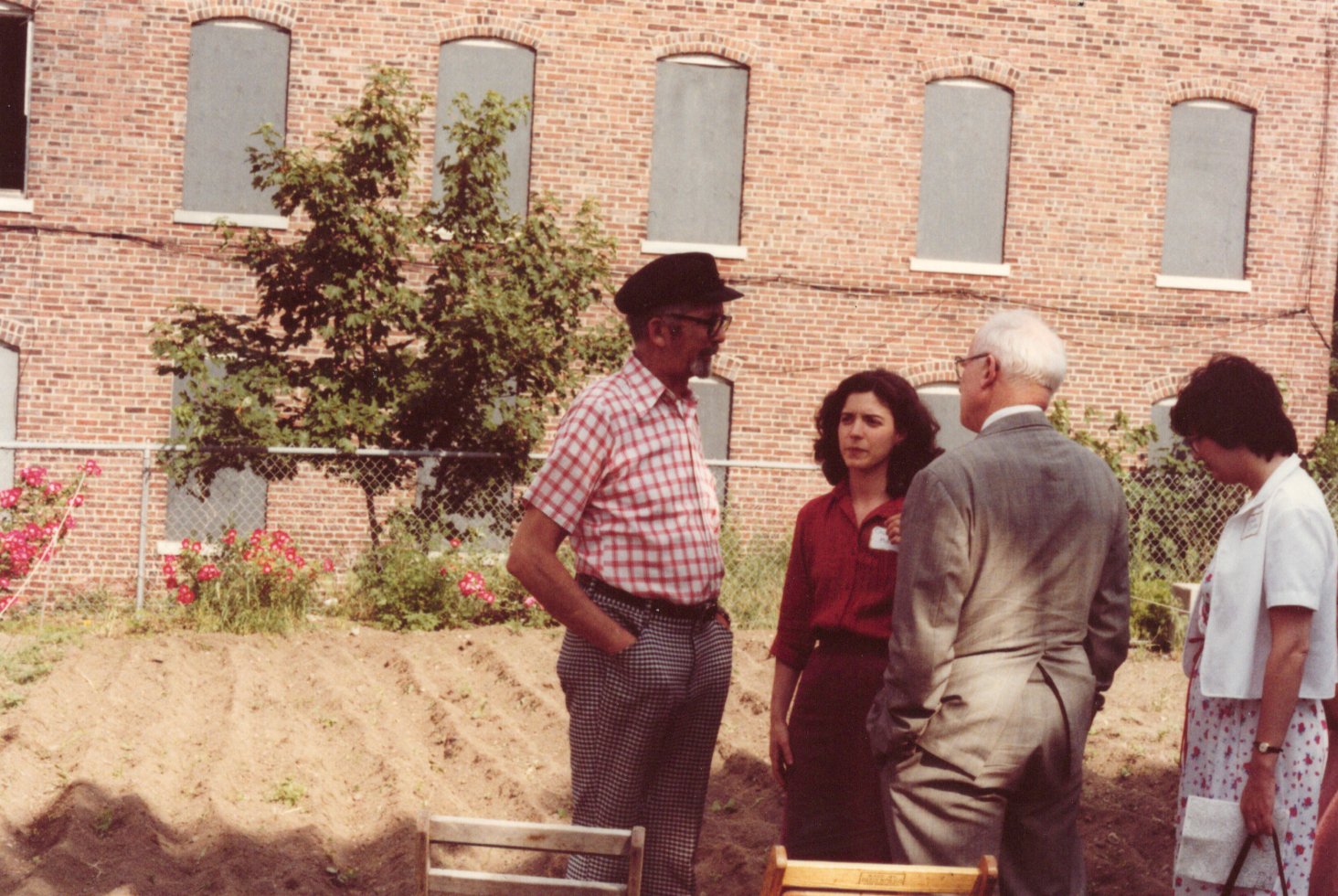 a 1980s photo showing a group of people talking outside an abandoned building and the site of an upcoming community garden