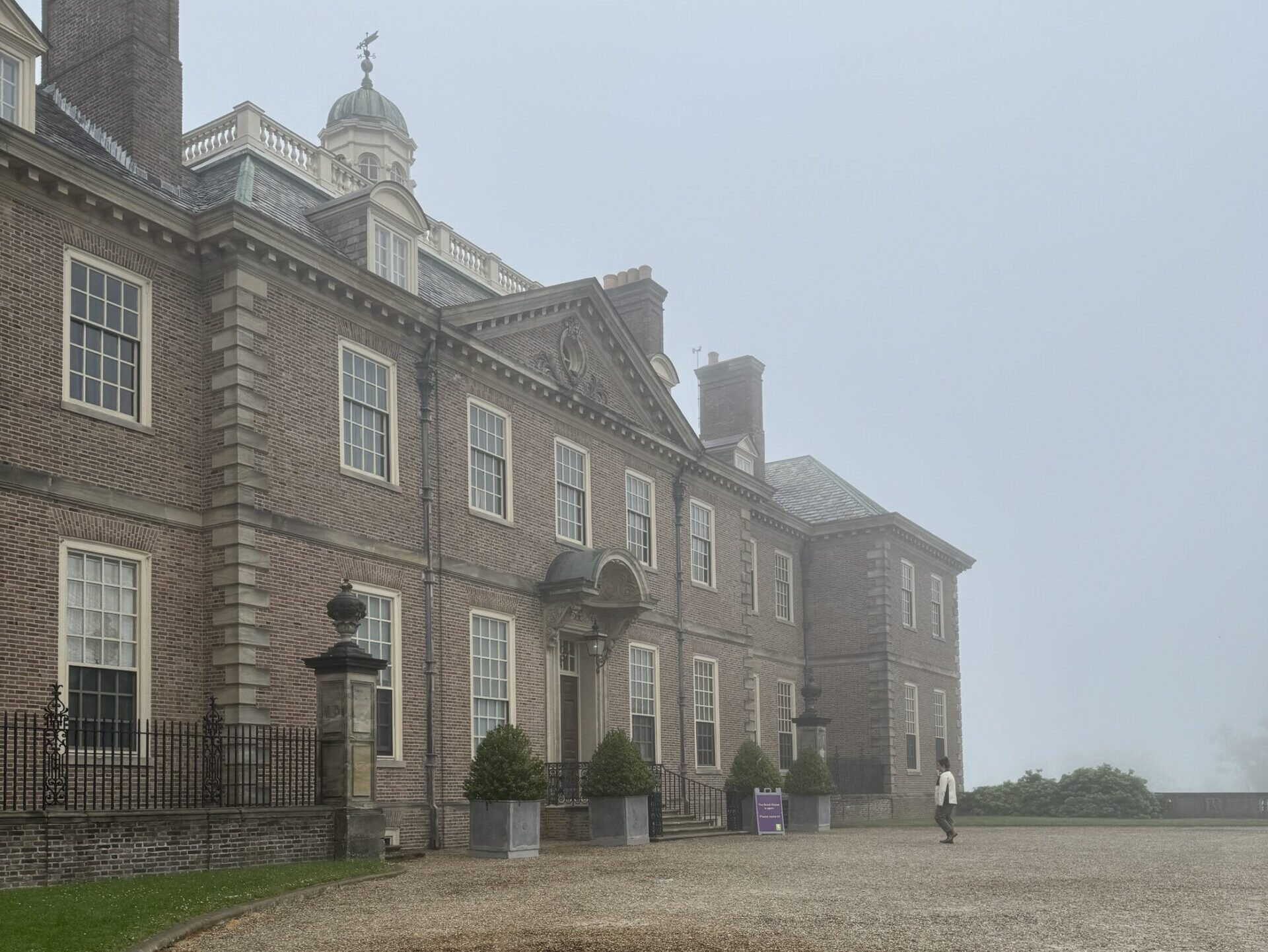 An estate made of stone sits on a pebbled drive in the fog.