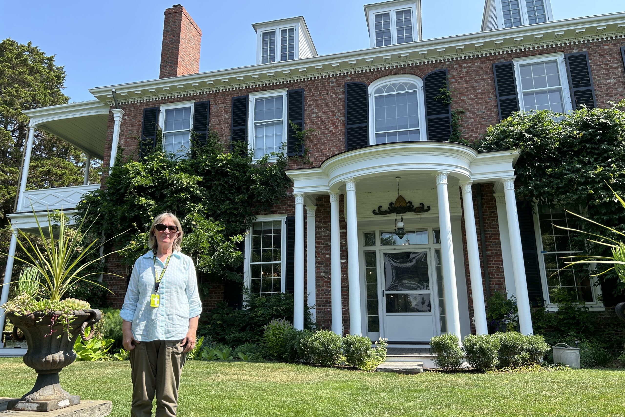 Volunteer House and Gardens Tour Guide Heather Ritcher stands in front of the historic house at Long Hill.