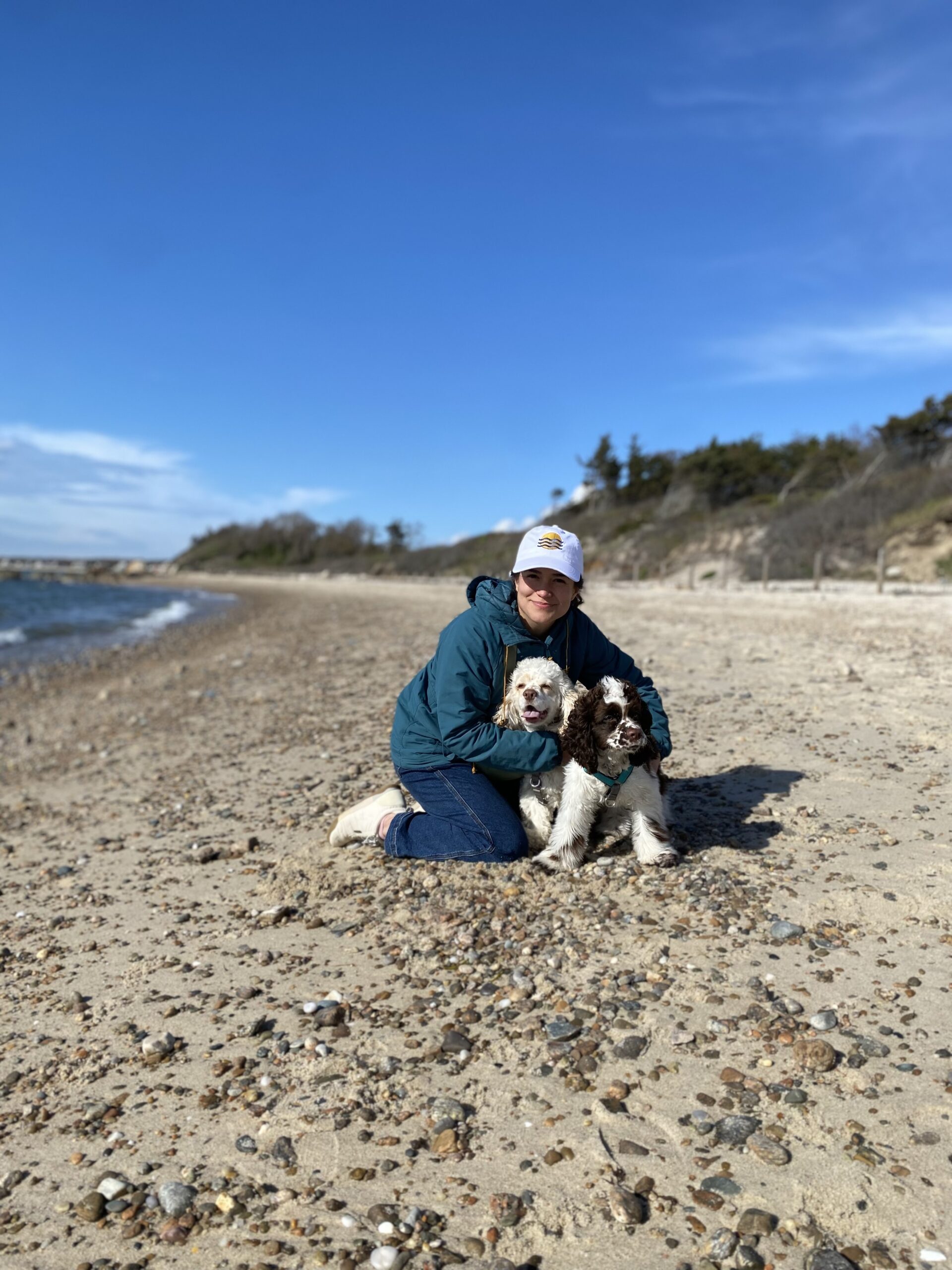 A staff member smiles on a beach with her dogs