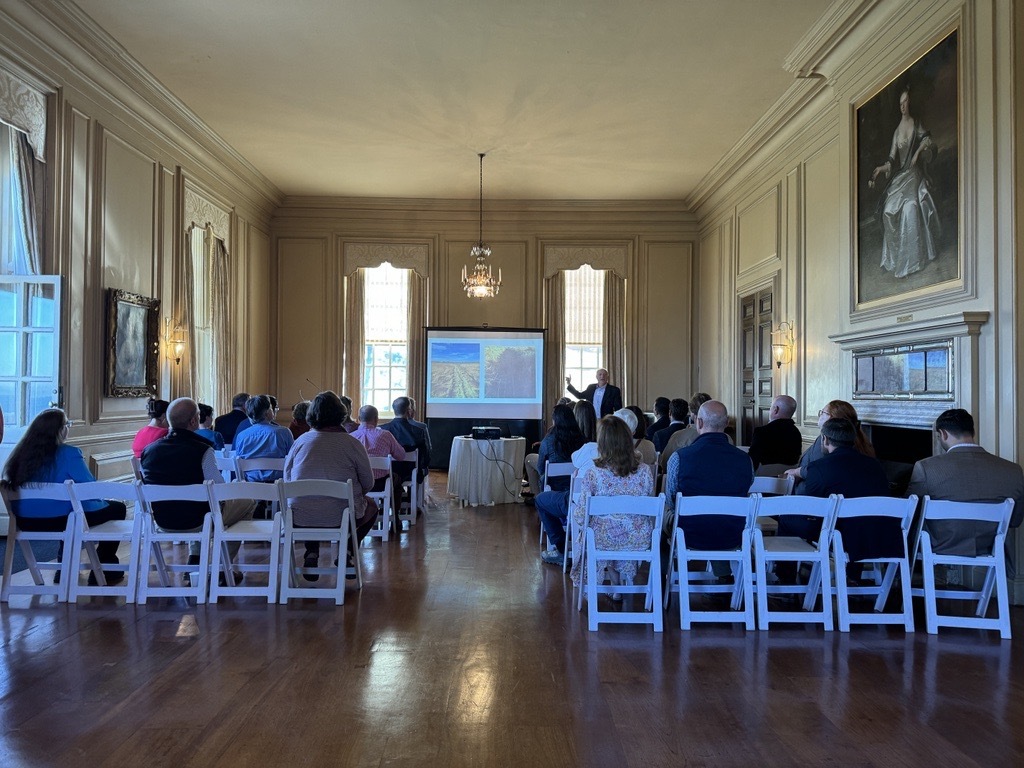 The ballroom in the Great House at Castle Hill is filled with chairs with people sitting facing away from the camera watching a lecture