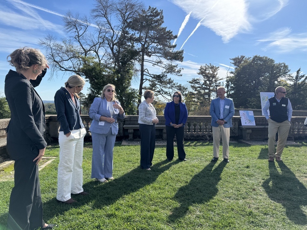 Several people stand facing an audience on a green lawn outside the Great House at Castle Hill