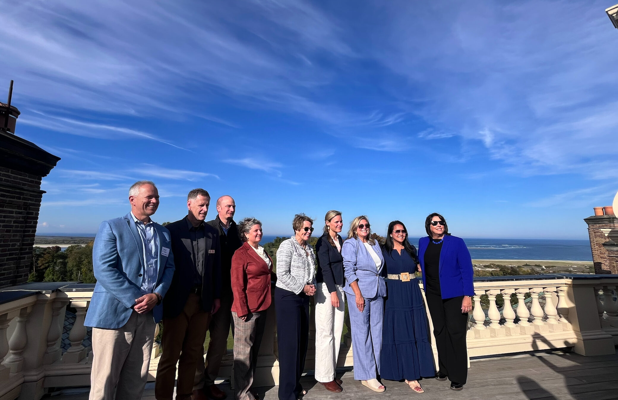 A group including MA Governor Maura Healey and Lt. Governor Kim Driscoll pose on the roof of Castle Hill