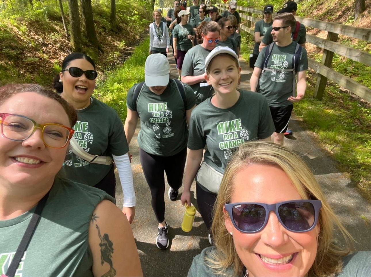 A woman snaps a selfie of participants in Hike for a Change walking along a trail.