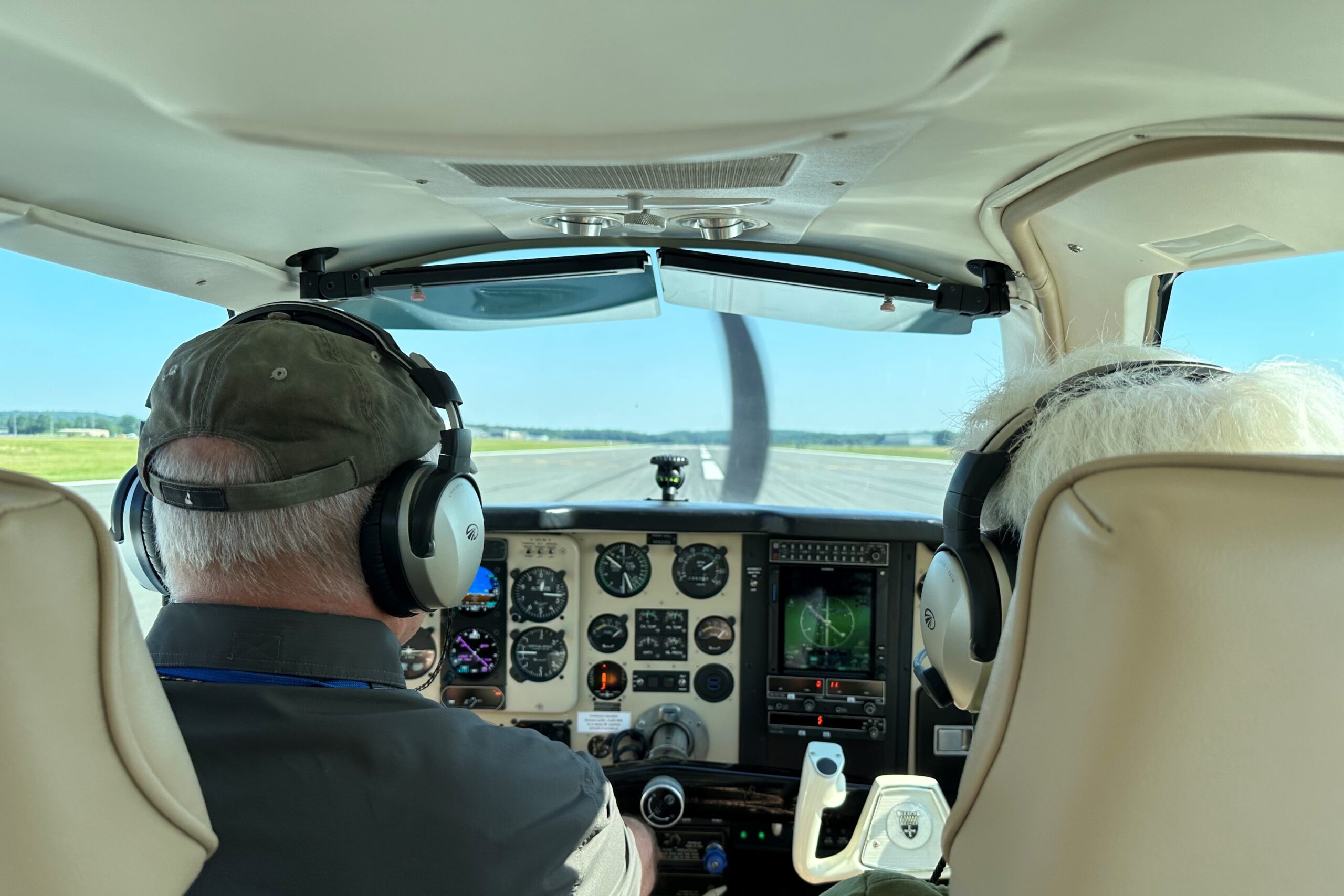 Two people in the cockpit of a small plane before takeoff, the backs of their heads facing the camera.