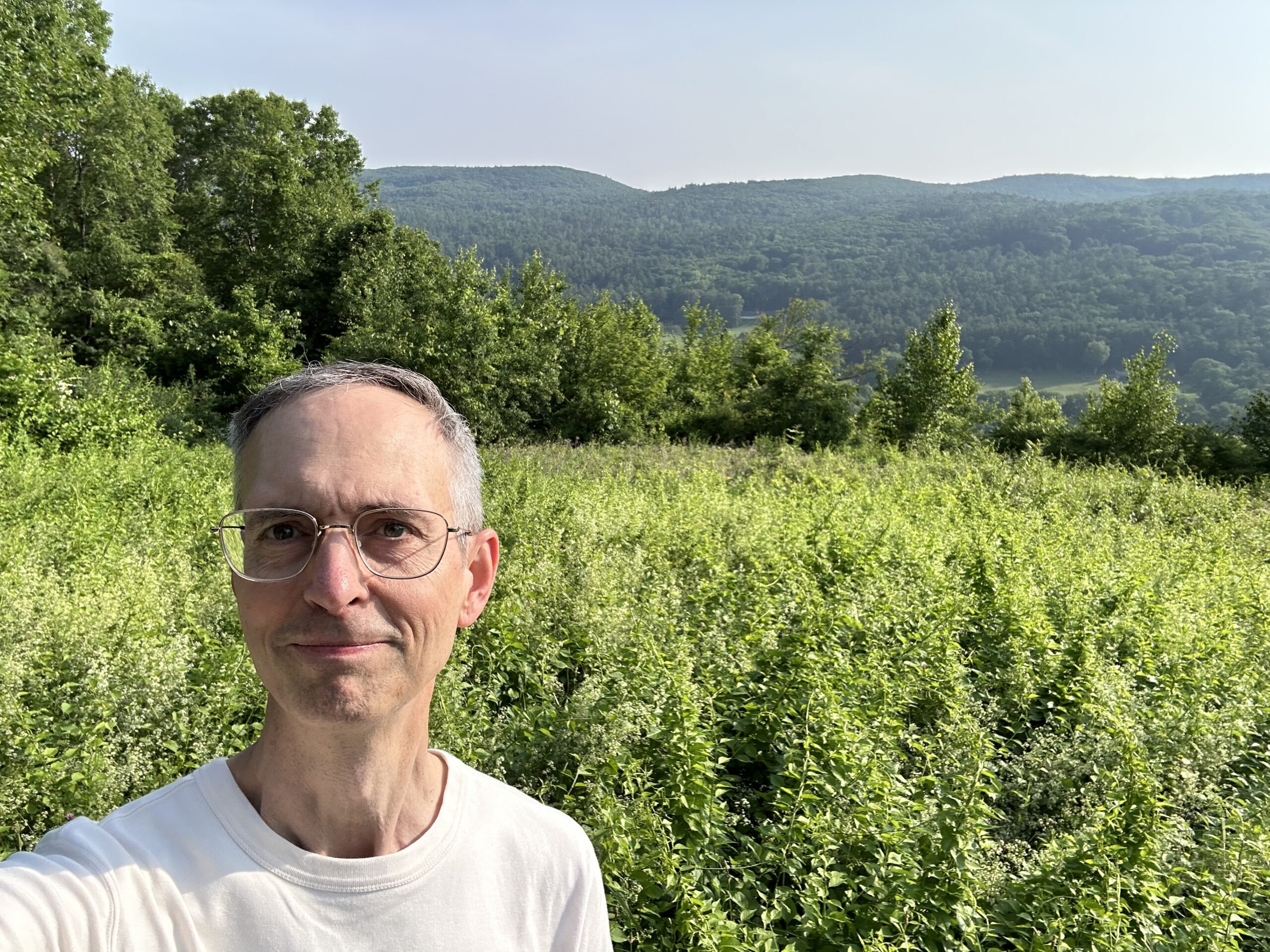 a white man stands in front of a grassy field with rolling hills in the back ground