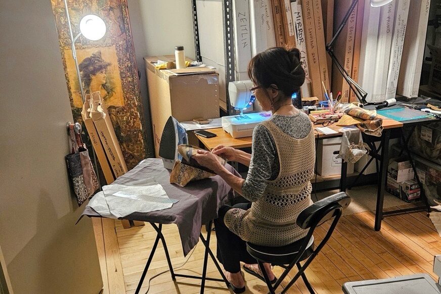 Artist Misako Litt, with her back to the camera, crafts her bags in a workshop.