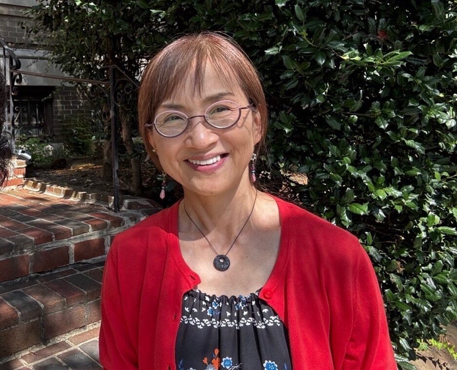 A woman with short brown hair and glasses wearing a red sweater smiles at the camera.