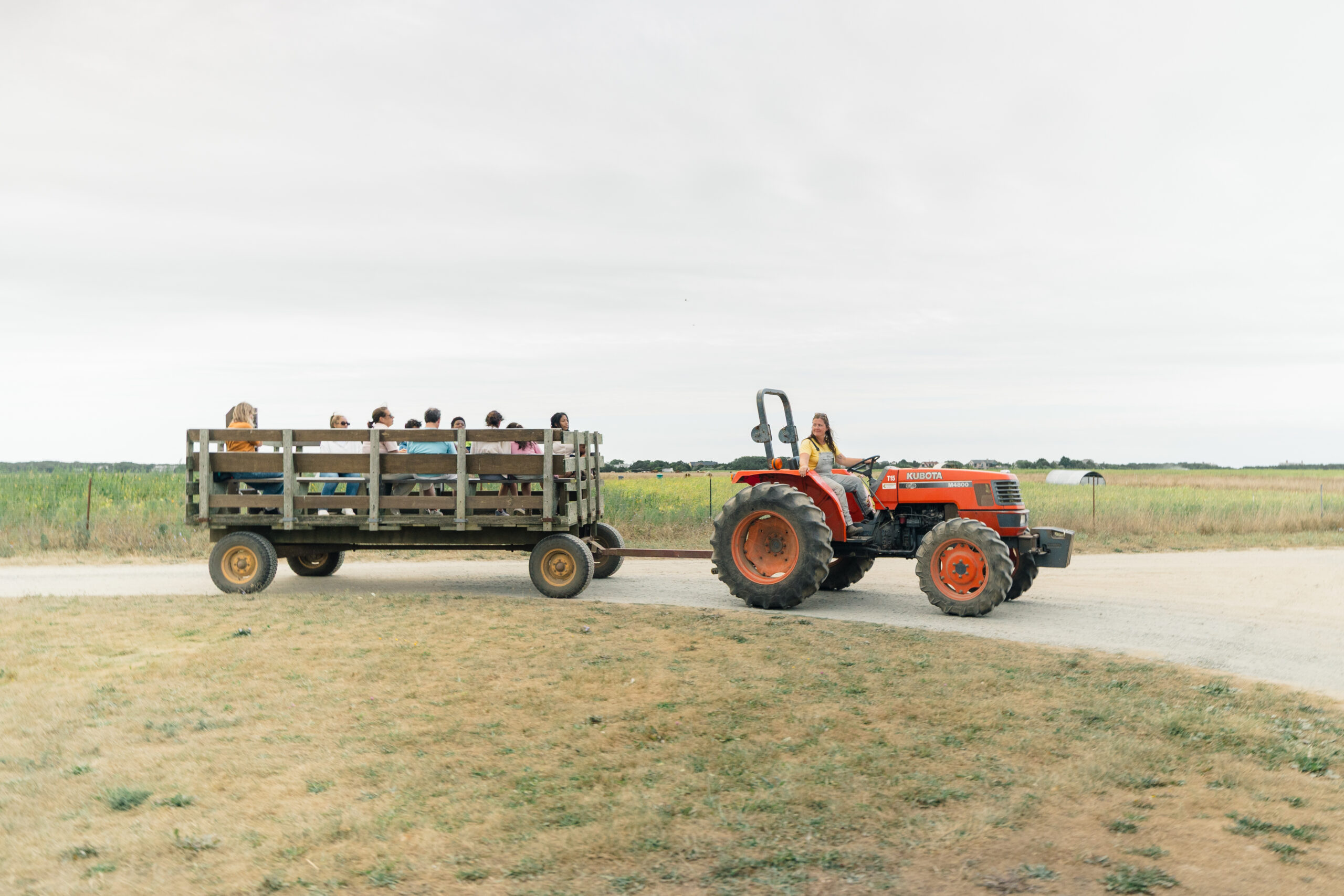 A red tractor pulling a trailer that is holding several people