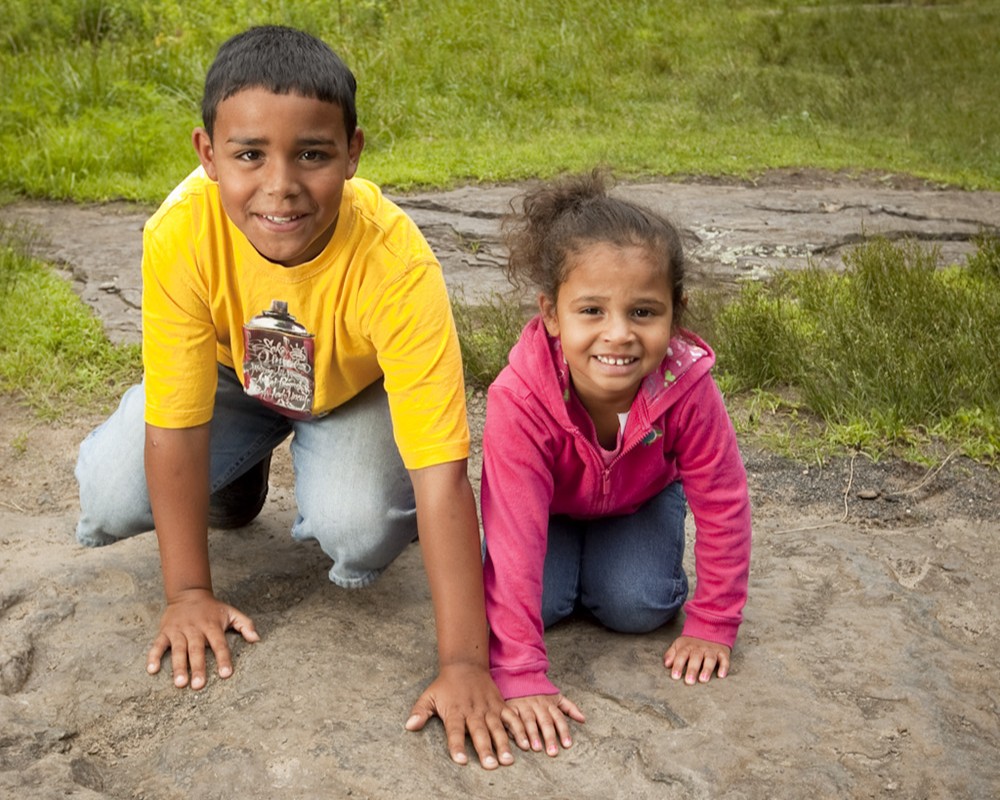Two kids touch a dinosaur track at Dinosaur Footprints in Holyoke, MA.