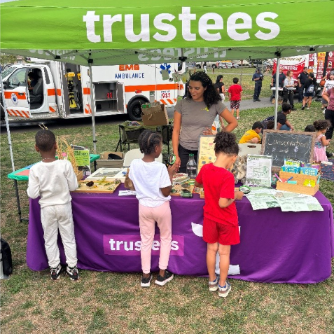 Children look at items on a table under a green tent